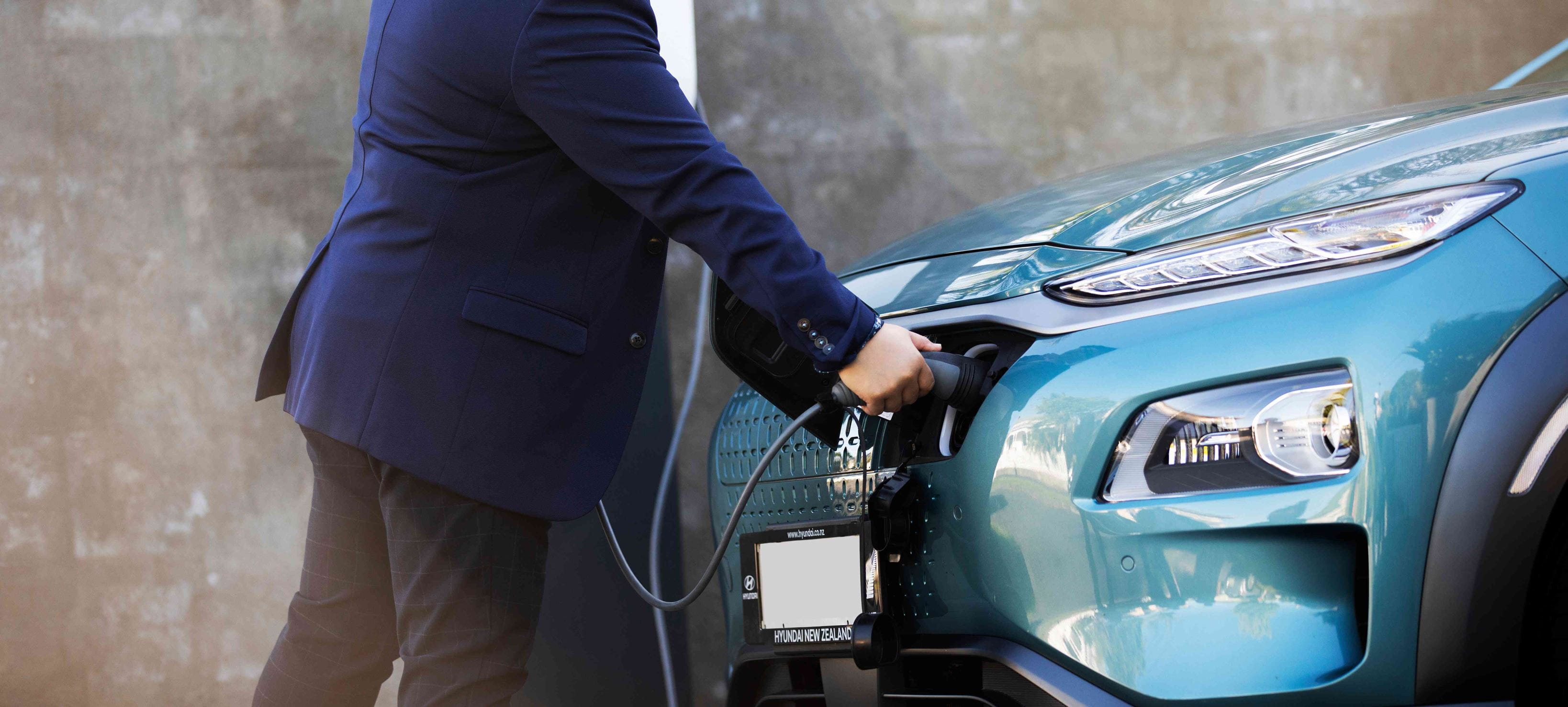 A man in a blue suit is charging an electric vehicle