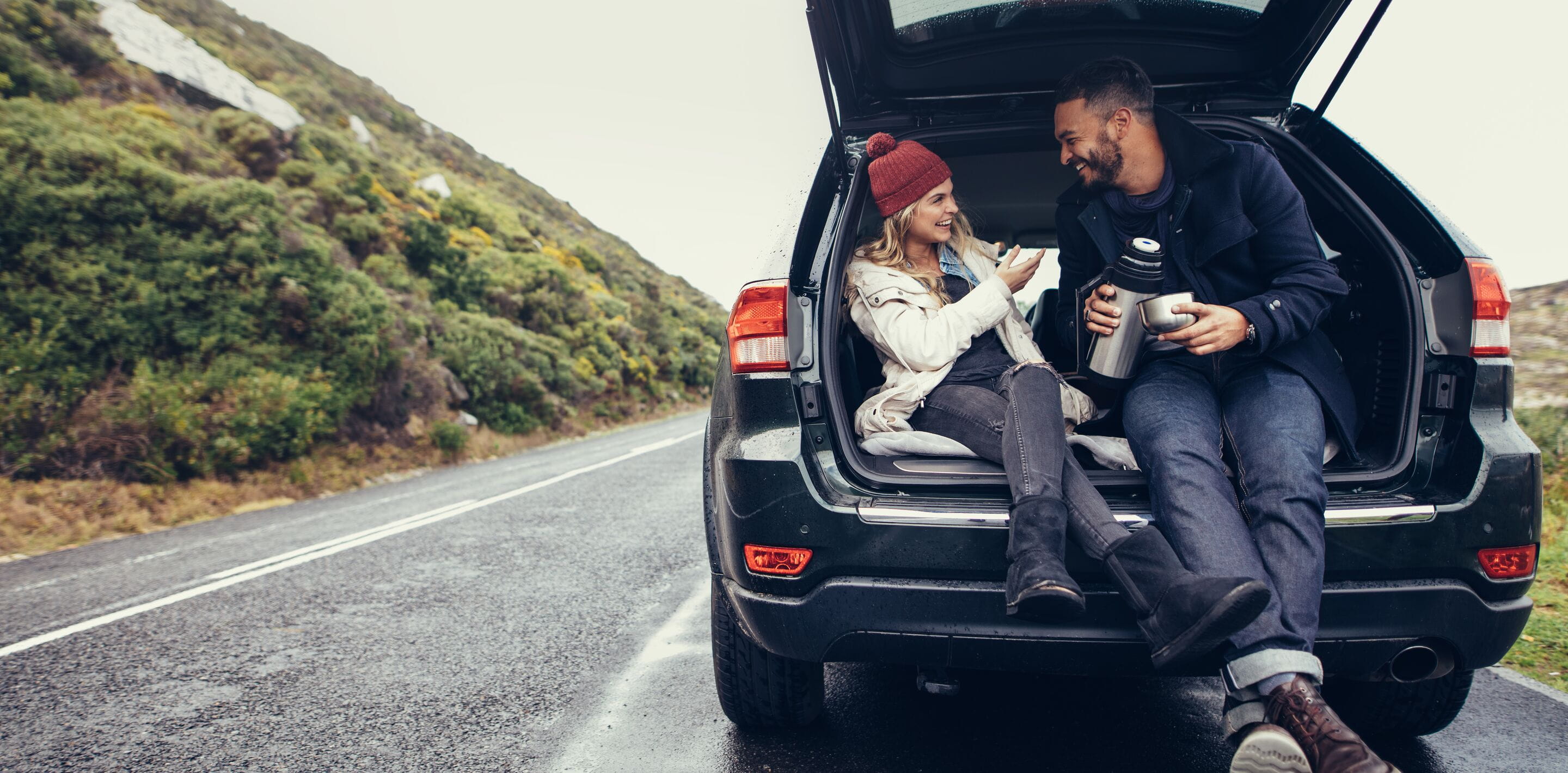 Woman and man sitting on the back of a car