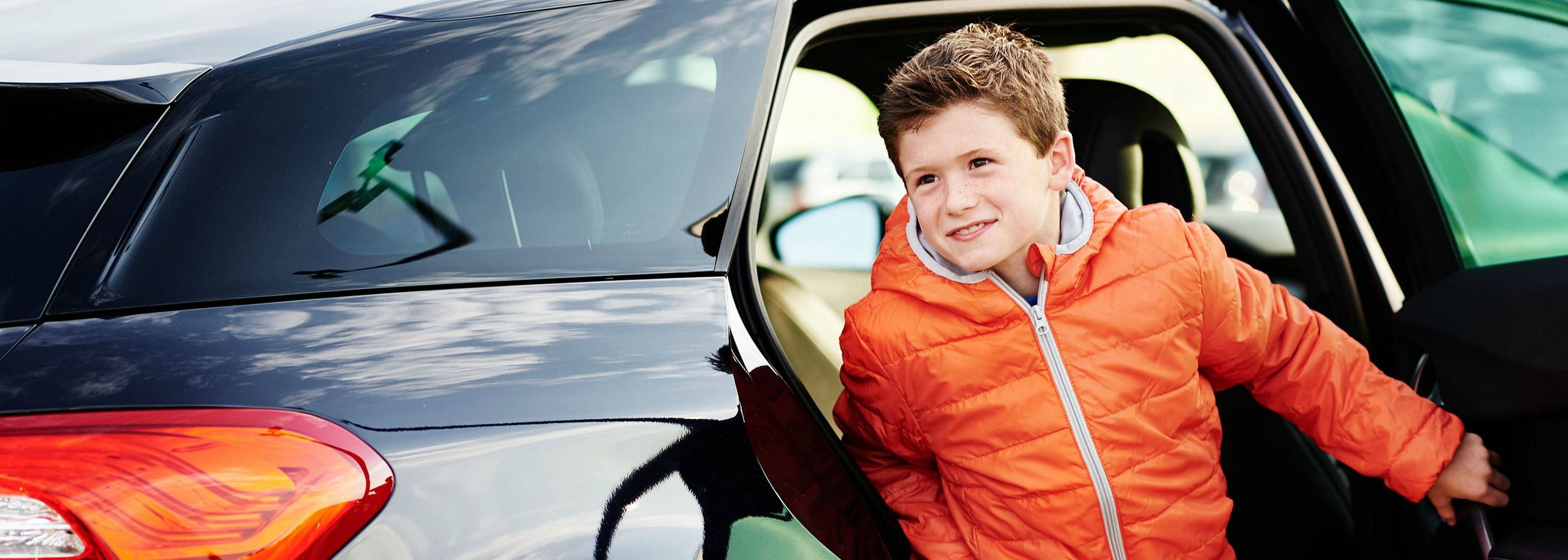 a child in an orange jacket gets out of the car