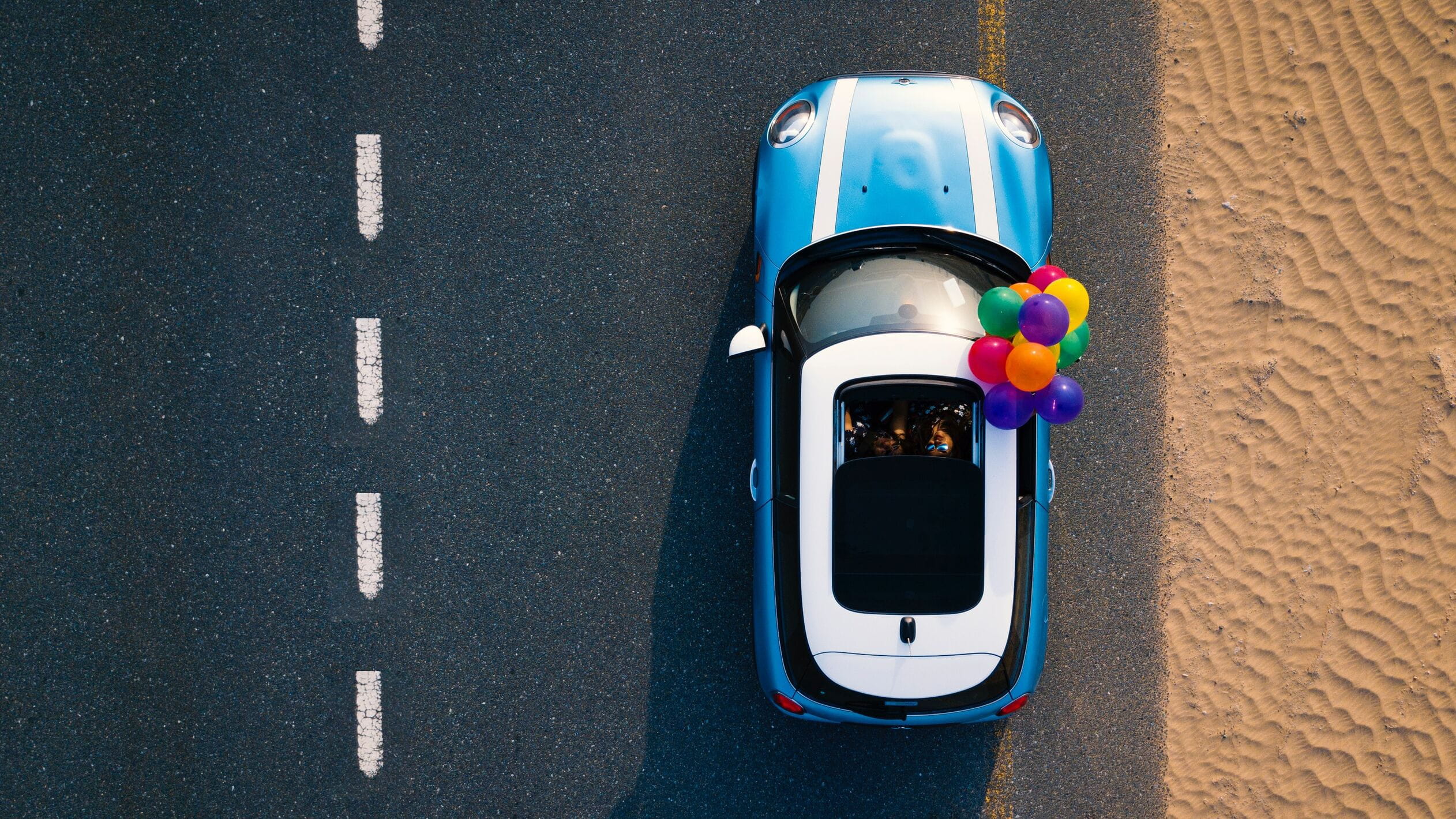 Car with balloons on road next to beach