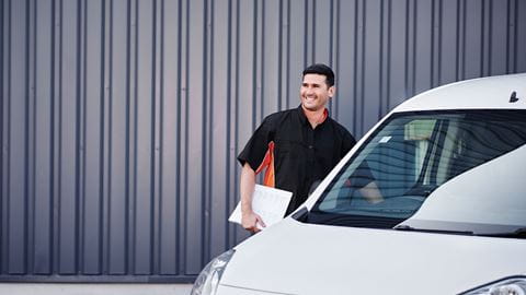 Sie liefern, weil wir liefern Lächelnder Mann steht neben Transporter