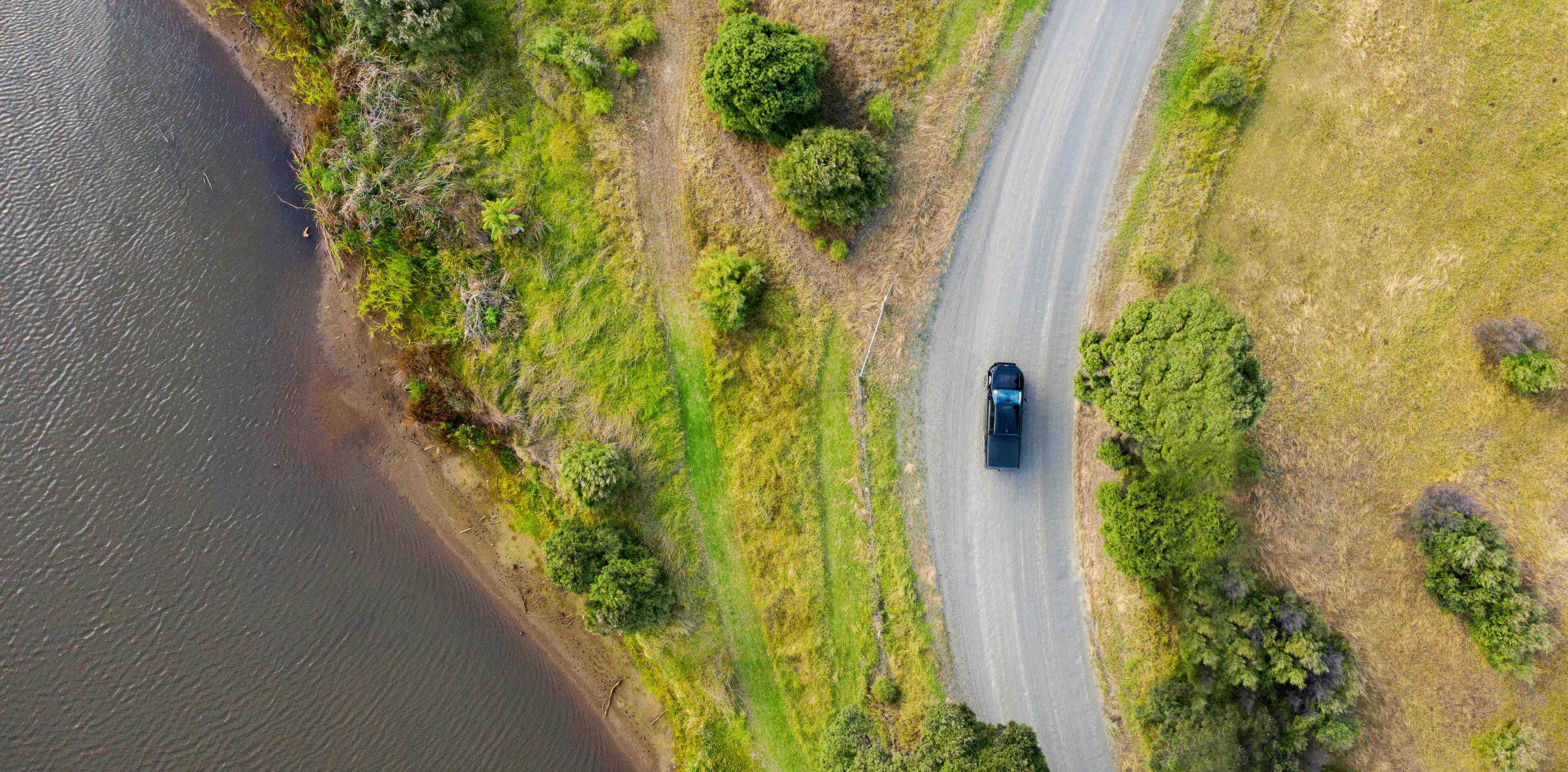 Aerial view of a car driving through the road by the lake