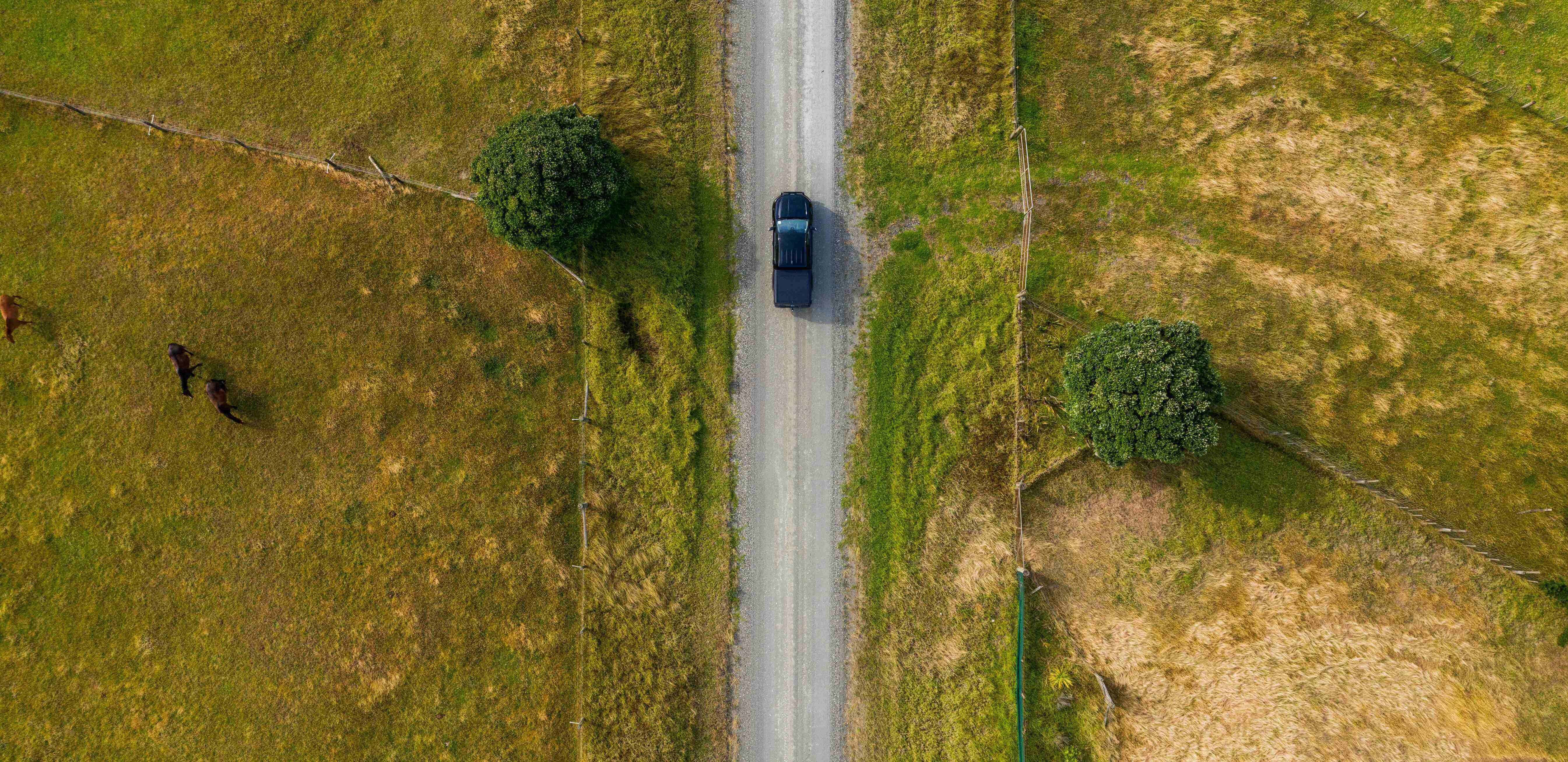 Aerial view of a car driving on a straight road surrounded by farmland