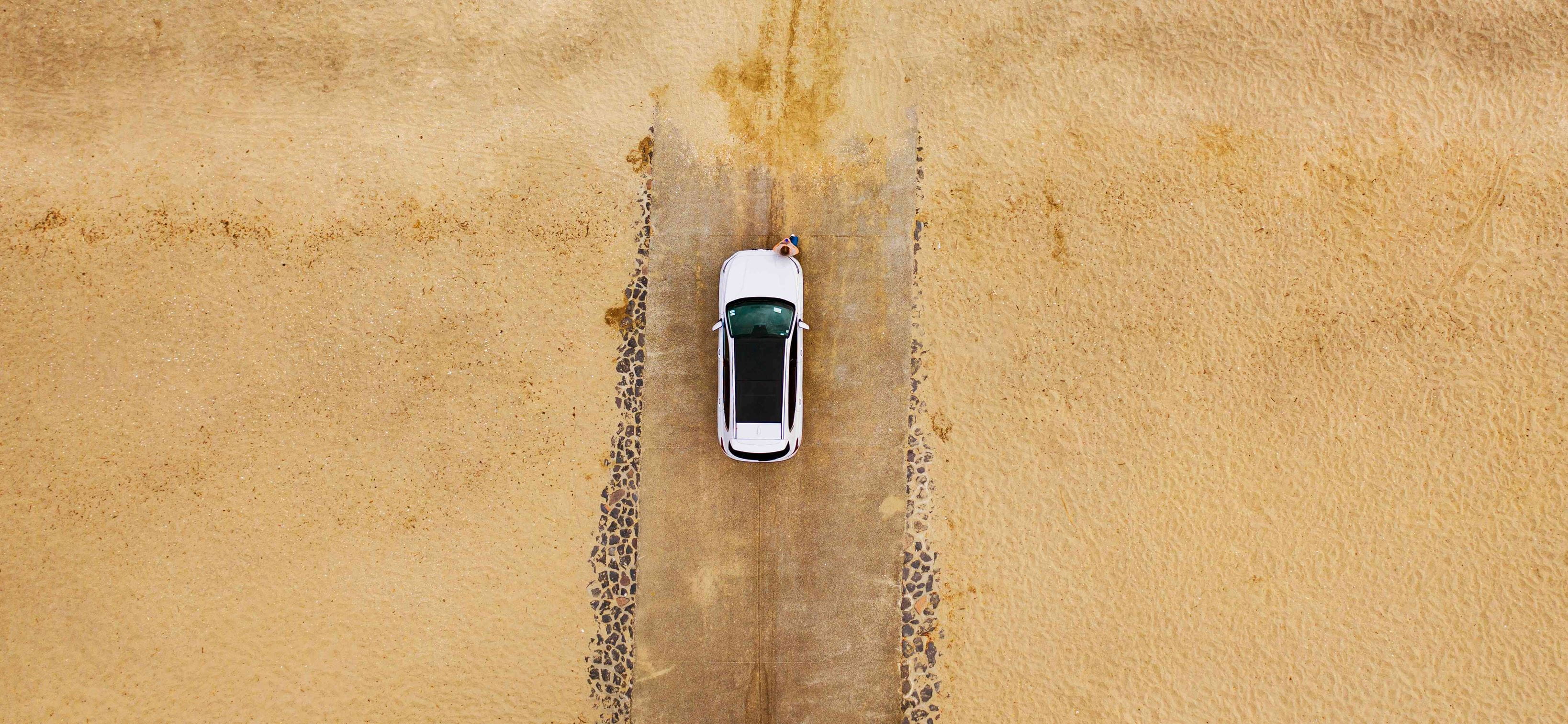 Aerial shot of a white car parked on the sand