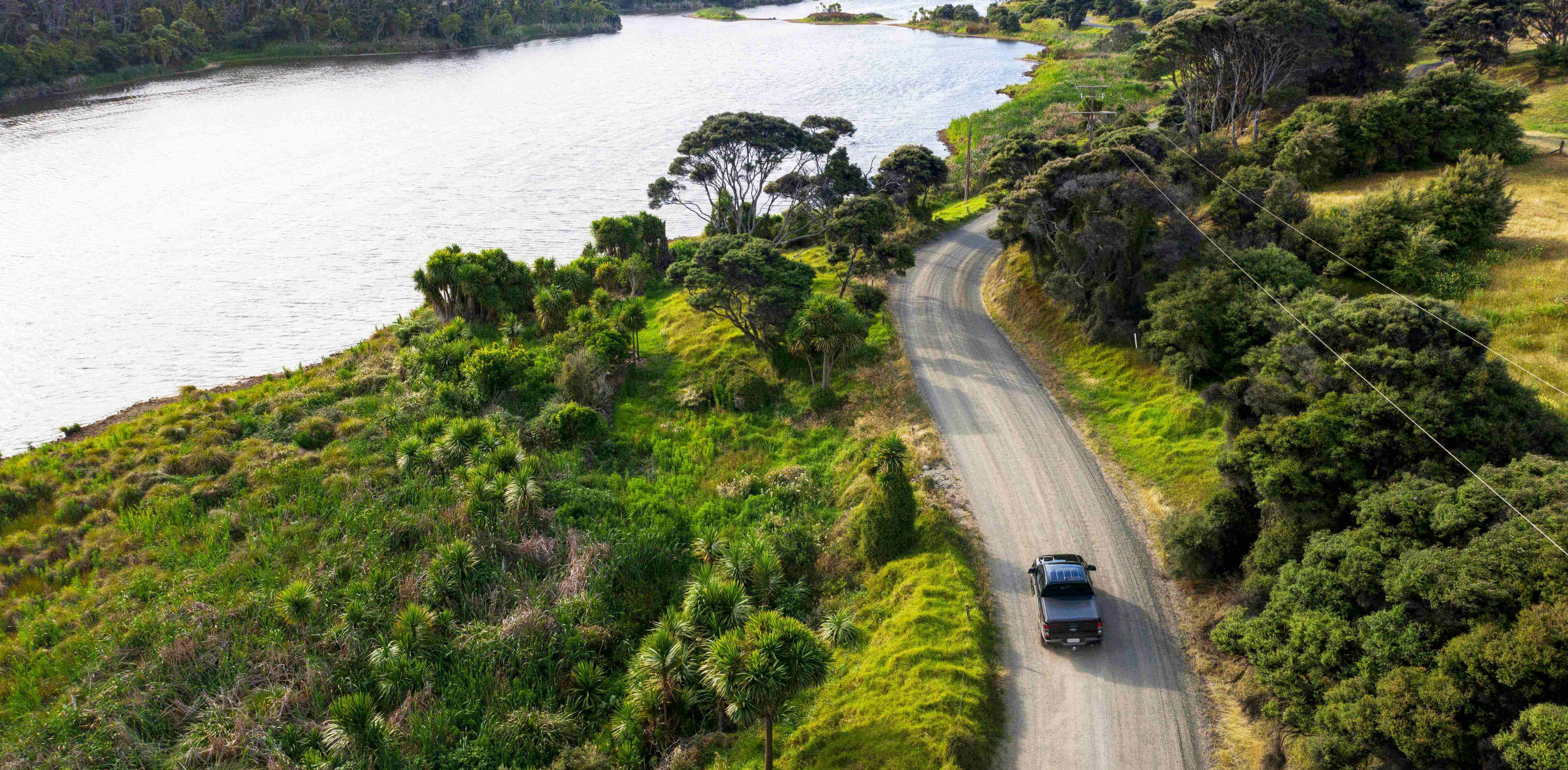 Aerial view of the rural road along the lake with a car passing through