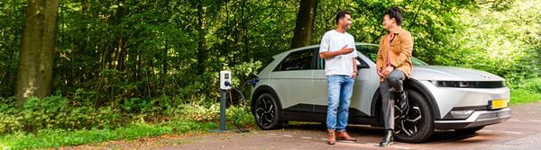 2 men standing next to the EV plugged in