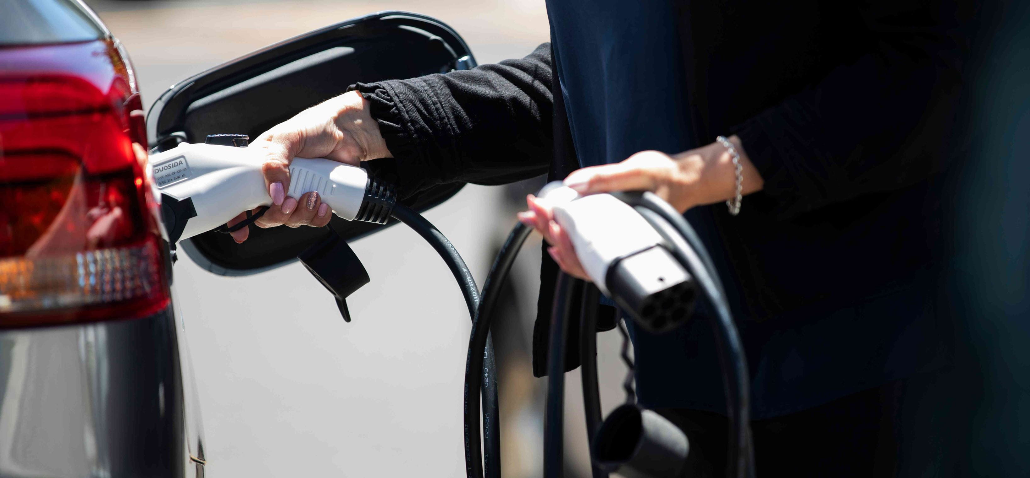 Close -up female hands holding power charging cable and charging an electric vehicle