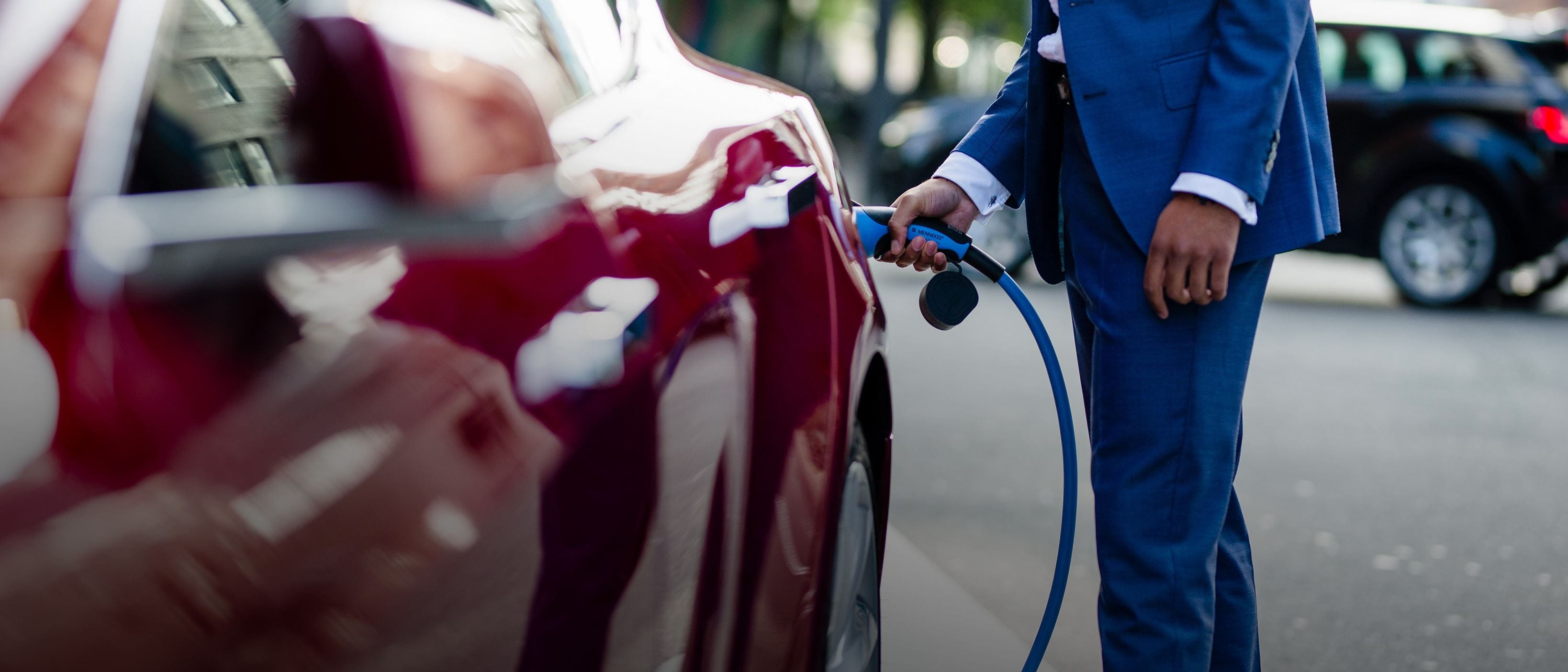 Close up - man in blue suit charging red Tesla