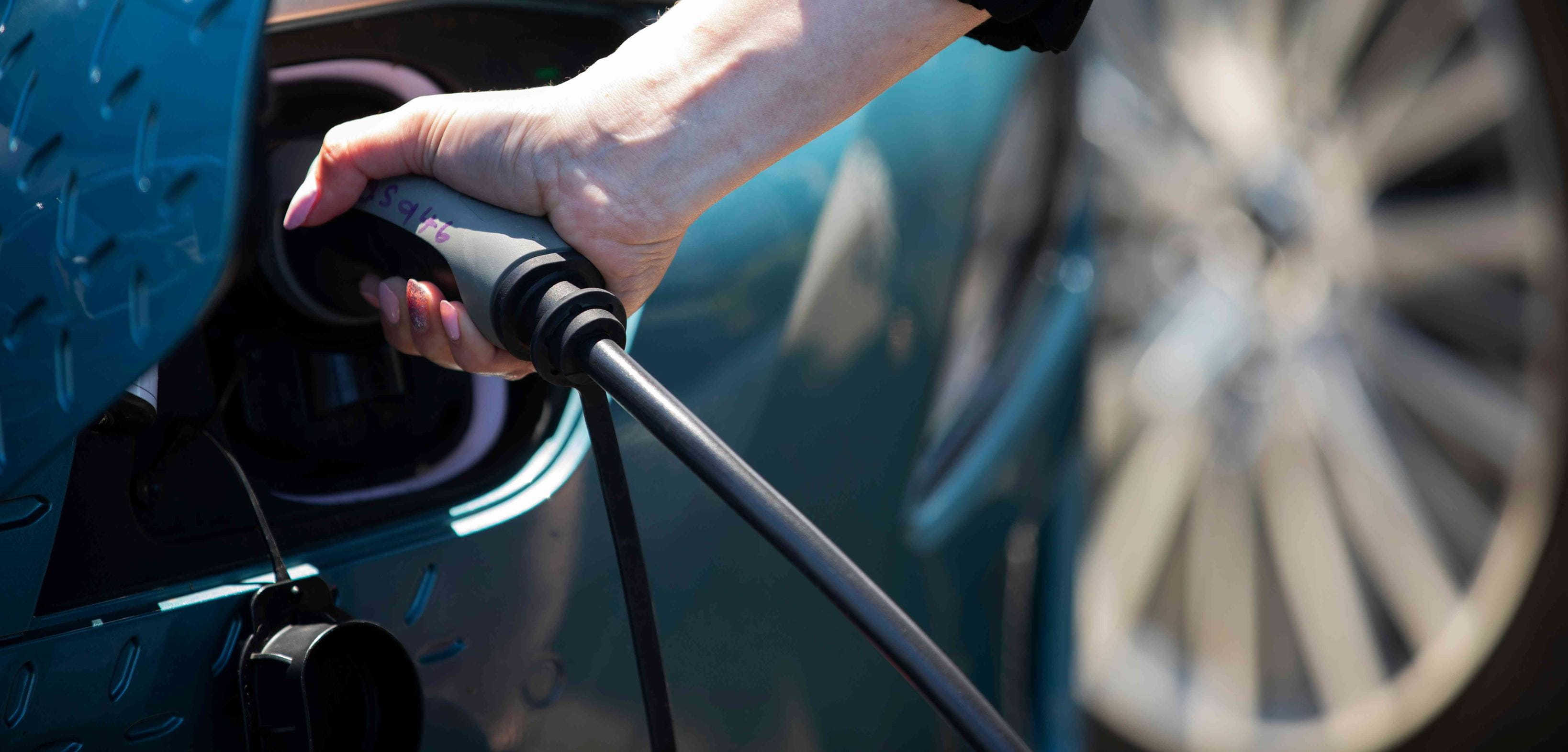 Close up of a male hand holding EV charging cable plugged into an electric vehicle