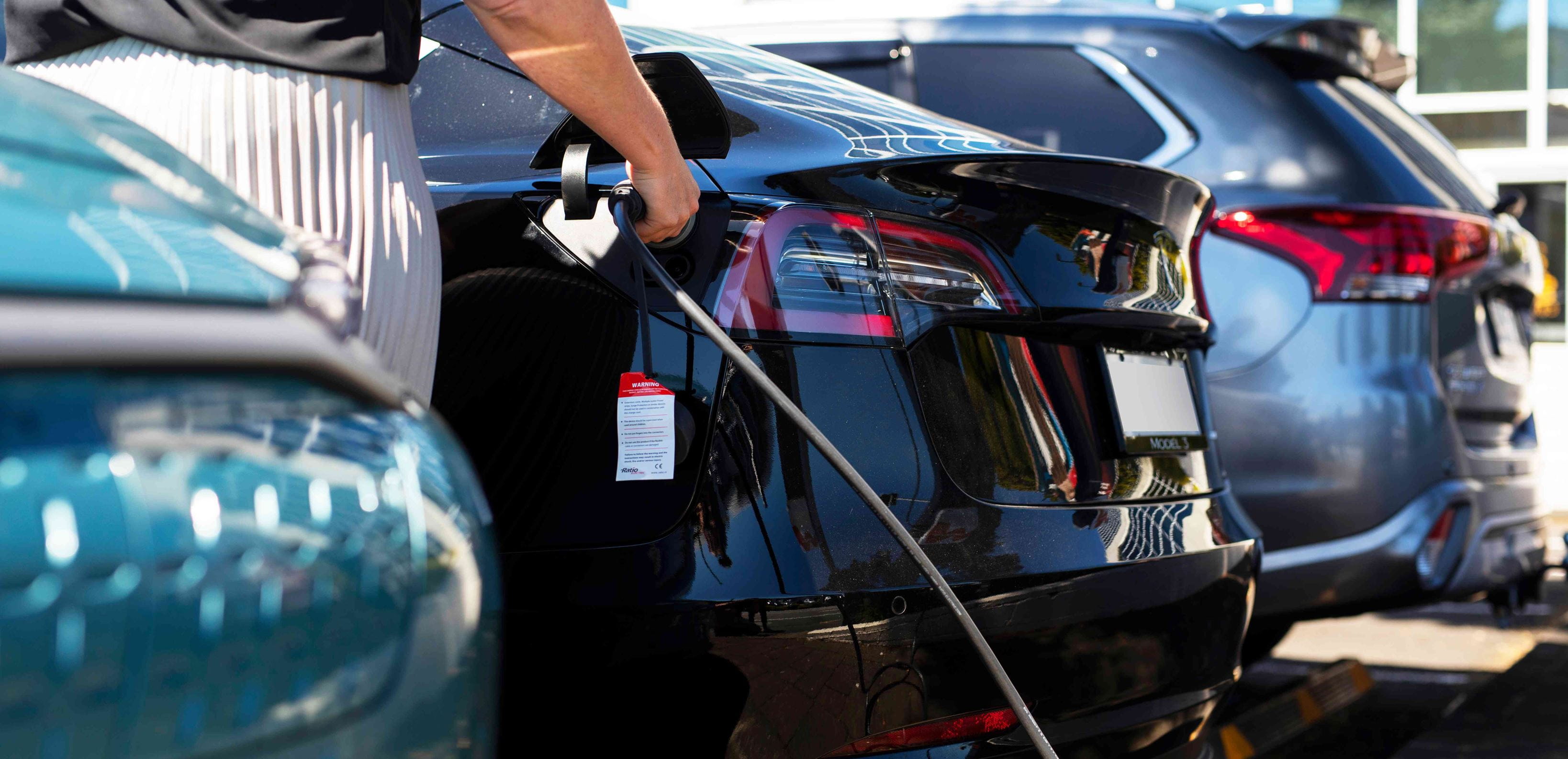 Woman charging black electric vehicle parked between two cars