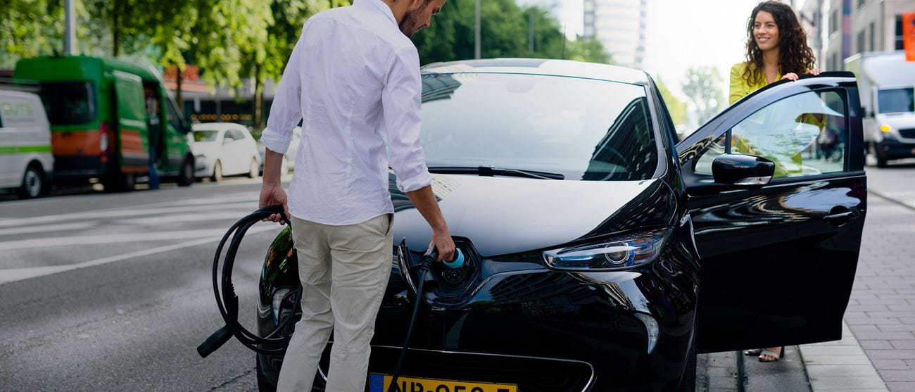 Man charging electric car - woman getting into car