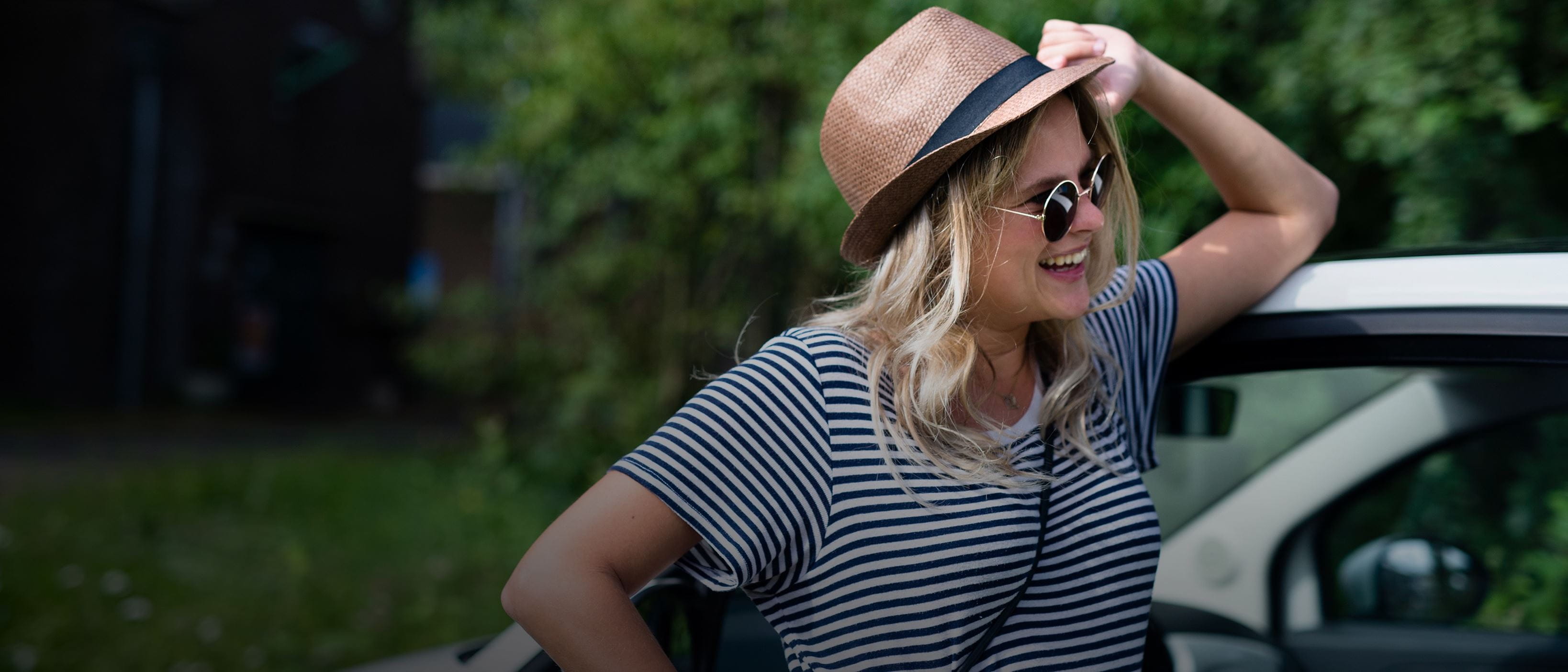 Woman in hat and sunglasses leaning on car