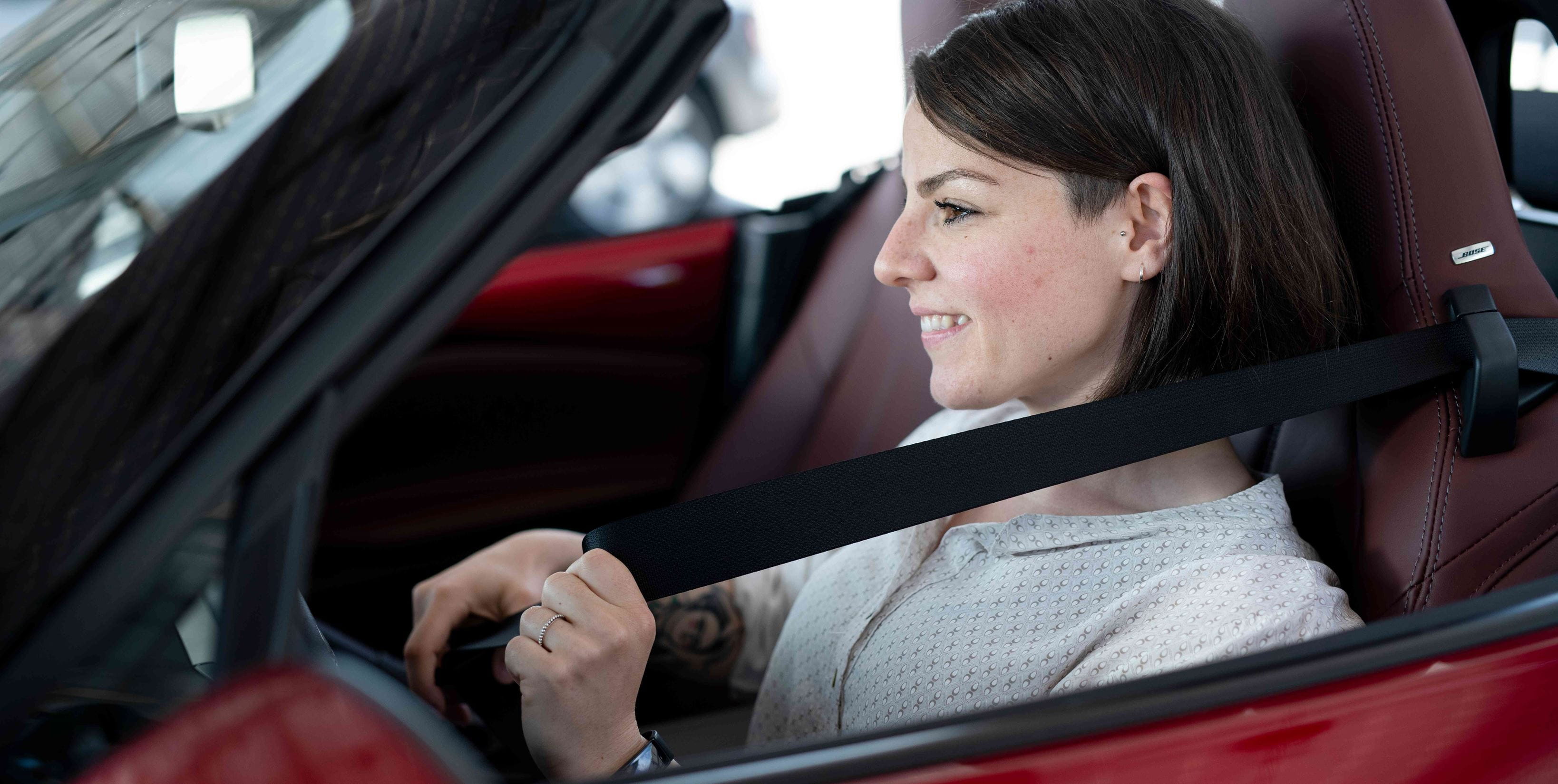 Woman putting on seat belt in red convertible